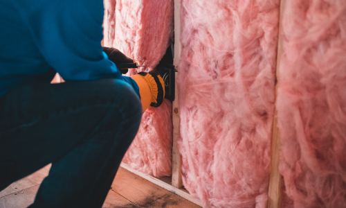 Pink insulation being rolled out and installed to a wall.