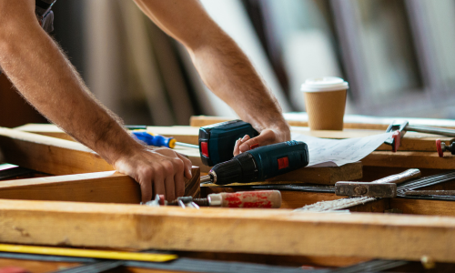 A close-up of a power drill being used to drill into lumber.